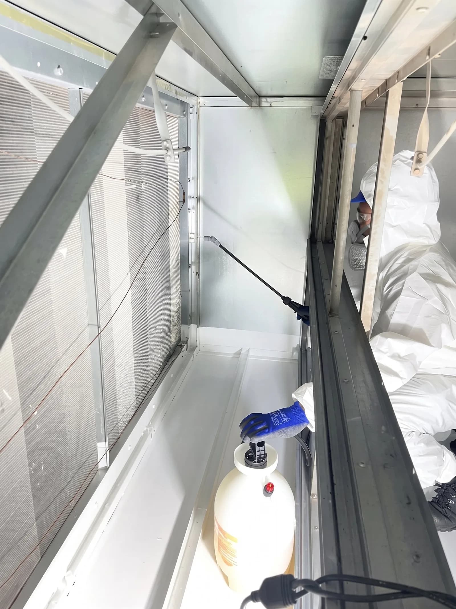 Urbacons technician in a protective suit and respirator applying a treatment inside a cleaned air handling unit