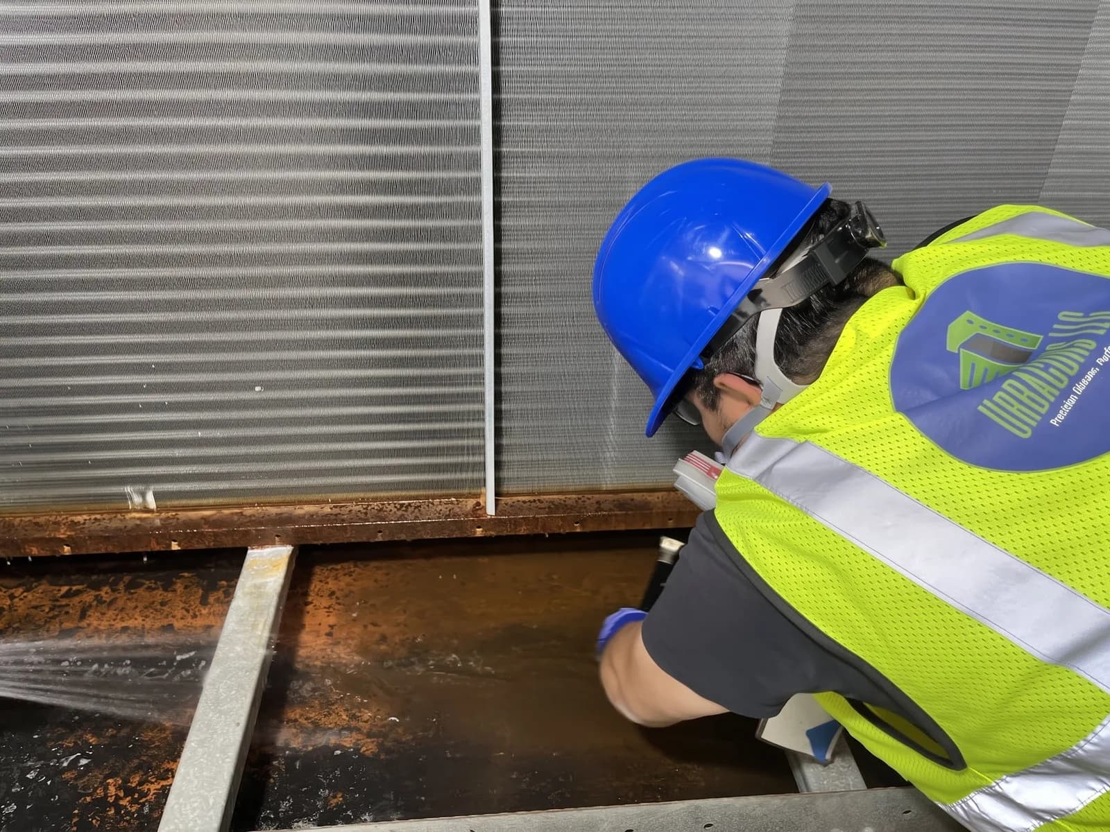 Urbacons technician rinsing a corroded condensate drain pan inside an air handling unit