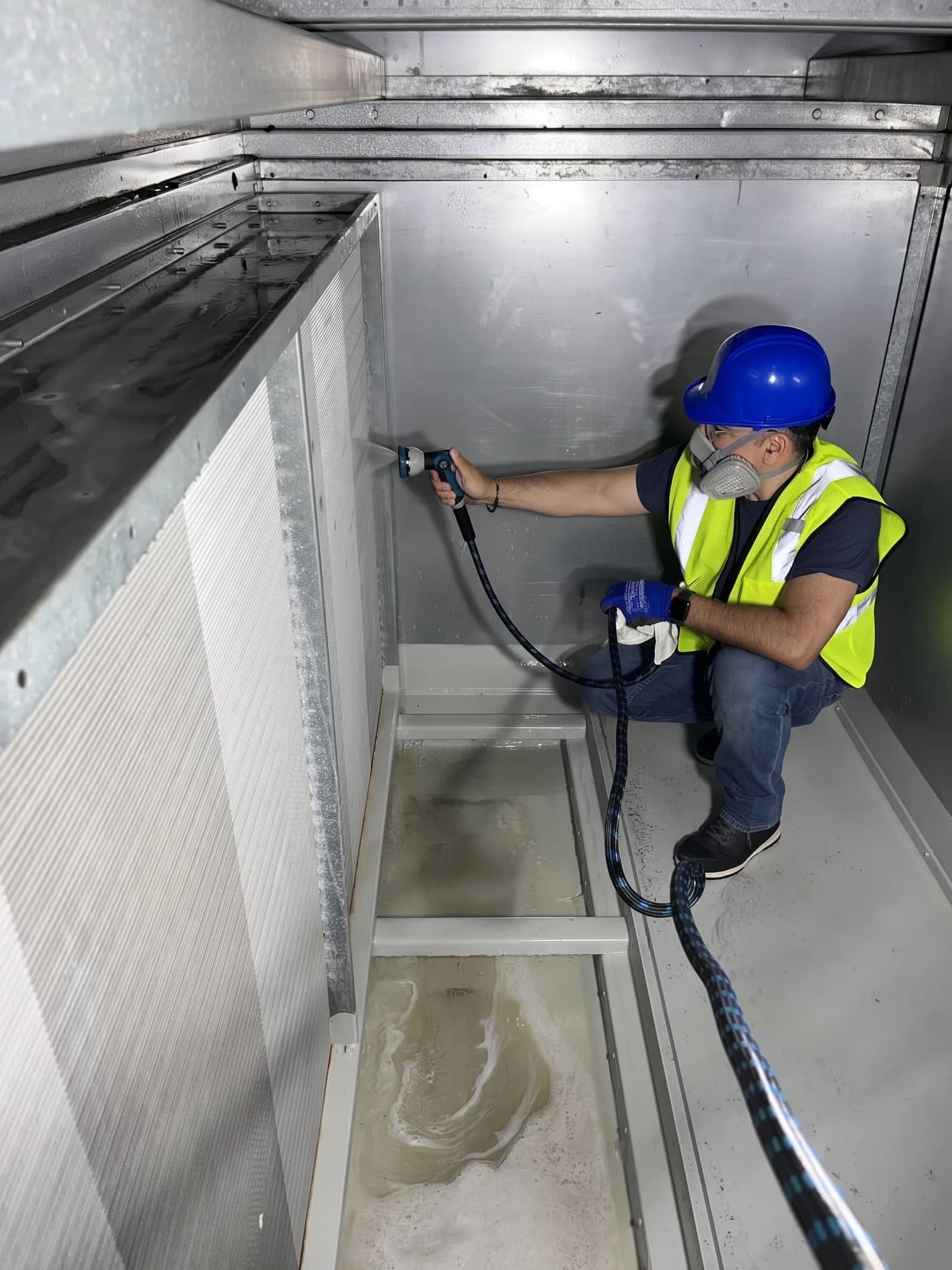Urbacons technician in a respirator spraying the interior of an air handling unit