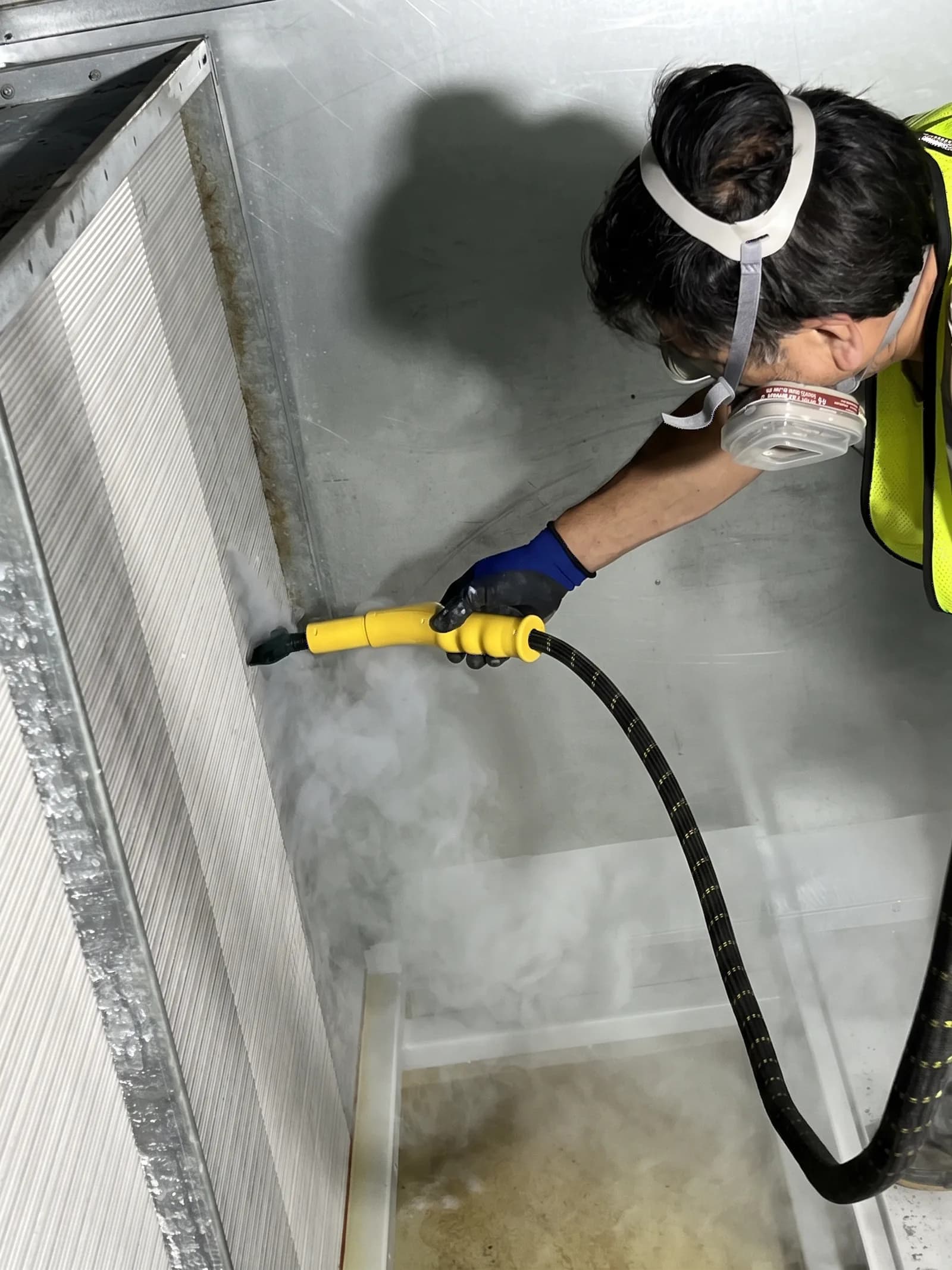 Technician steam-cleaning the coil of an air handling unit